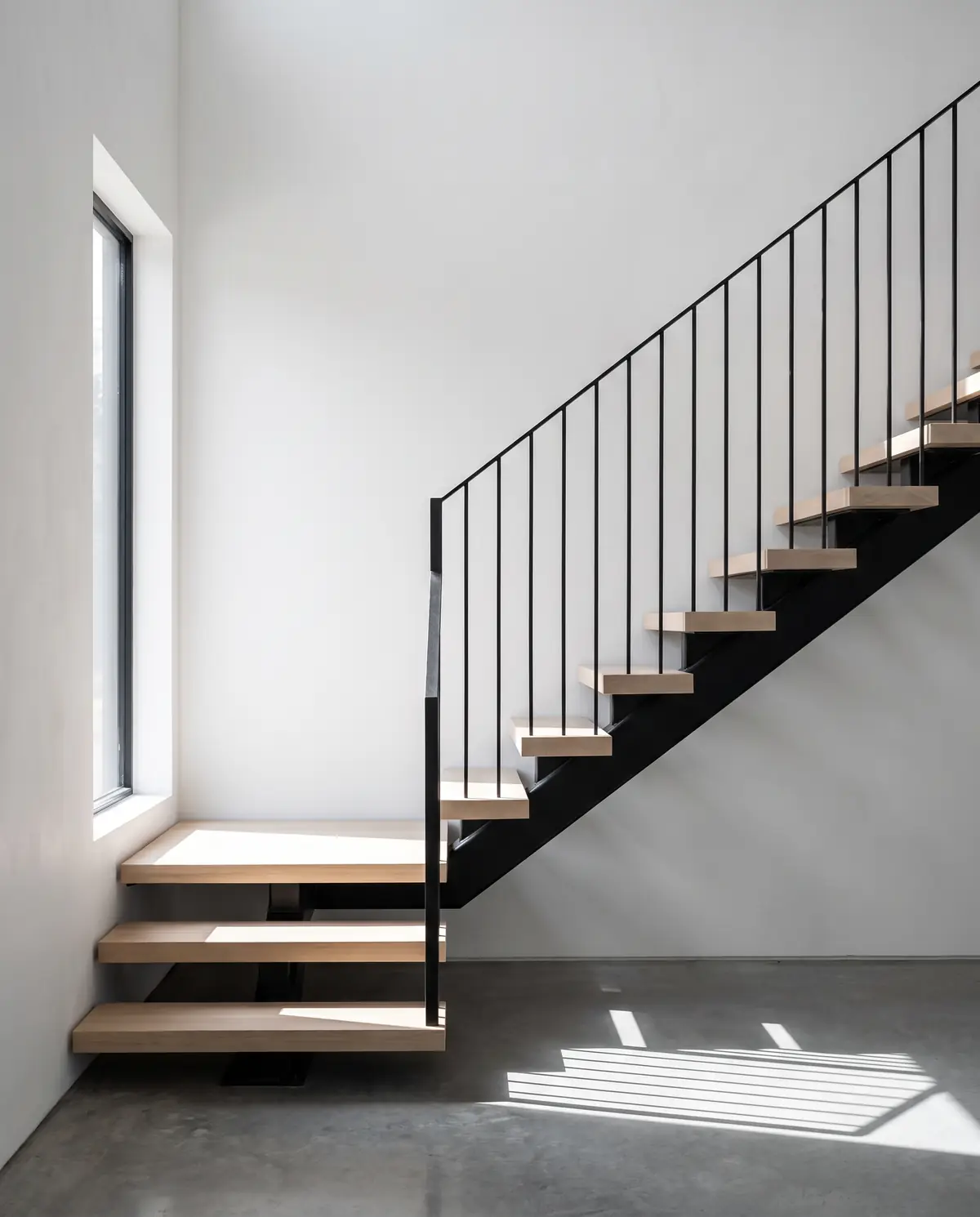 A floating white oak staircase with a blackened steel stringer against white plaster
